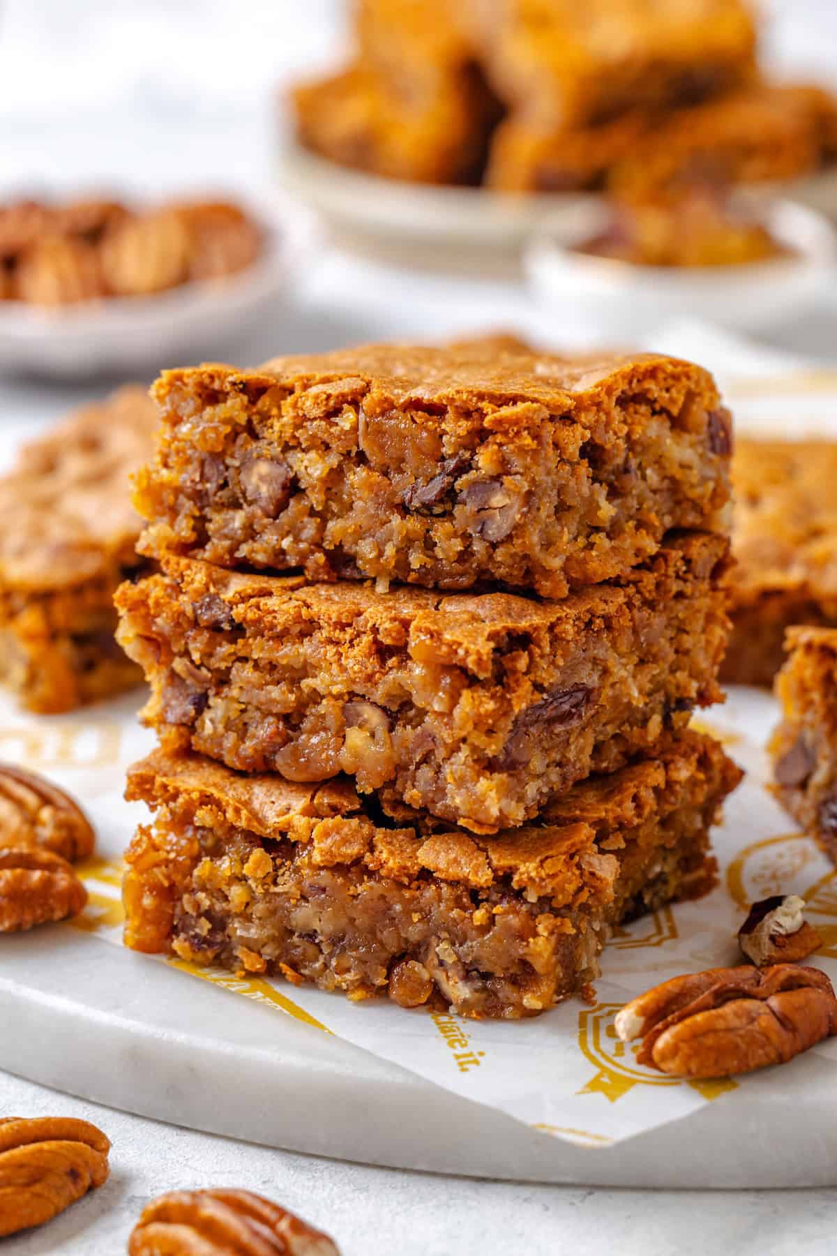 A stack of three square pieces of Southern chew bread on a marble slab with pecans scattered around.