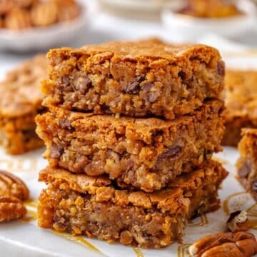 Close up of a stack of three square pieces of Southern chew bread on a marble slab with pecans scattered around.