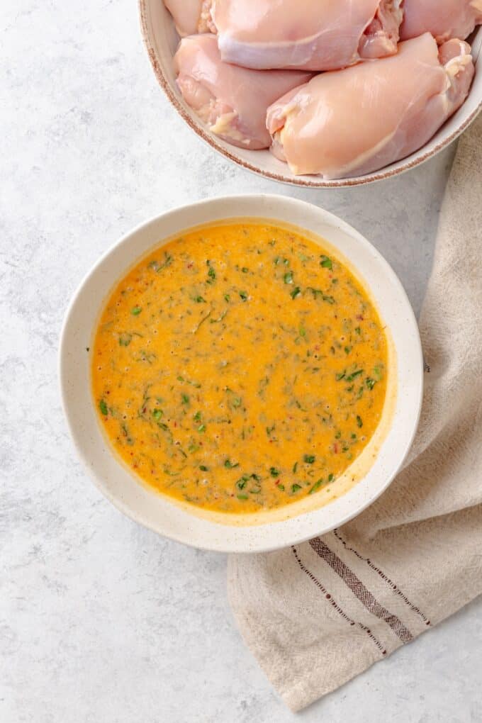 A coconut milk based grilled chicken marinade with red curry paste and lime in a white bowl.
