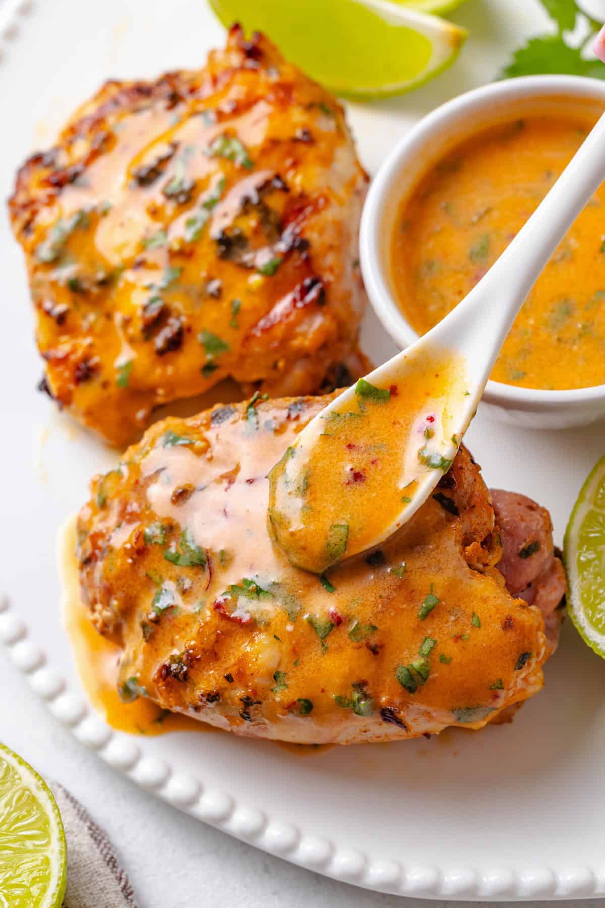 A spoon drizzling a coconut red curry lime sauce over grilled chicken on a platter.