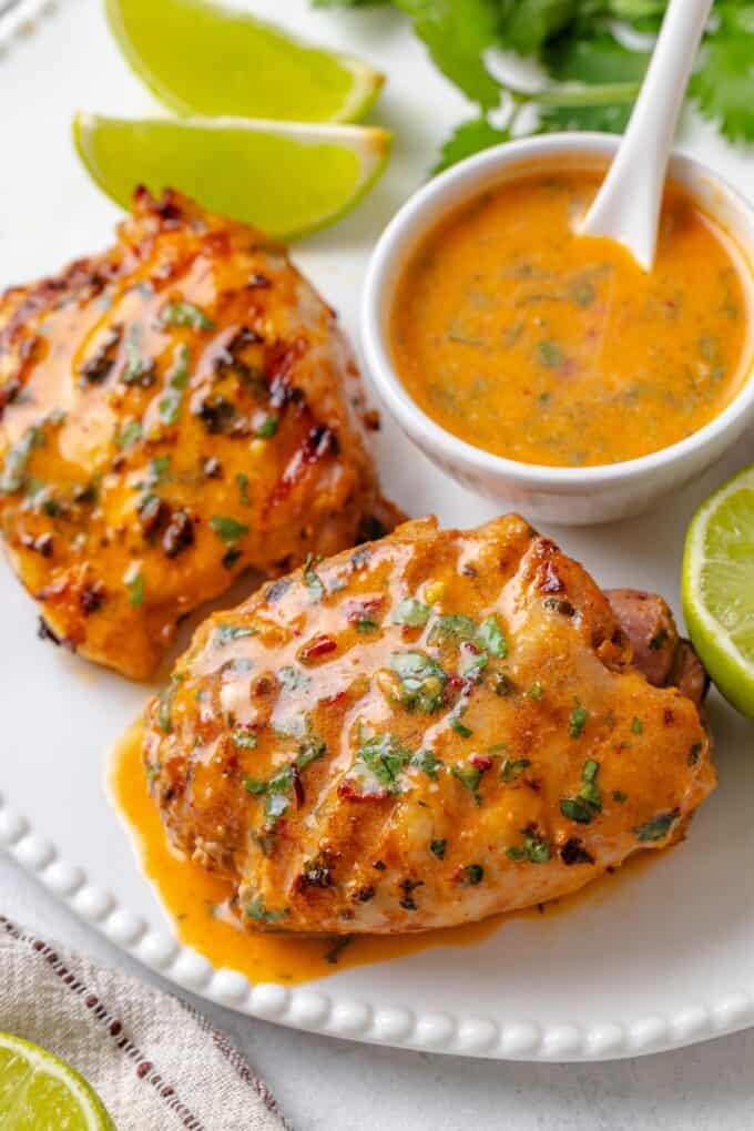 Grilled chicken on a white platter with a coconut milk based curry and lime sauce drizzled on top with extra to the side.