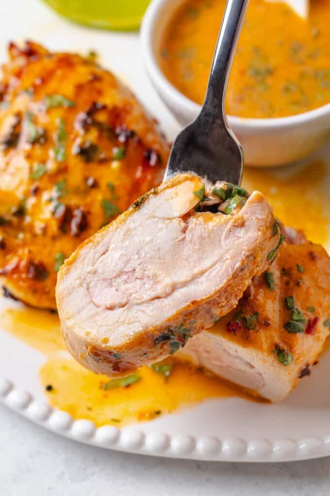 A fork holding up a slice of grilled chicken thigh with a coconut lime marinade from a plate.