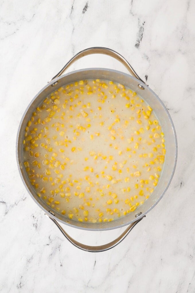 Yellow corn added to a potato mixture in a large pot.