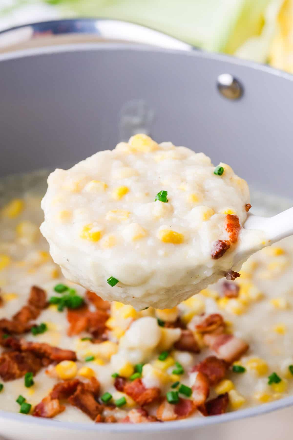 A scoop of corn chowder with bacon and chives being lifted out of a stock pot.