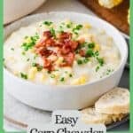 A white bowl full of corn chowder topped with bacon and chives on a plate with bread slices to the side with a green border and text around the photo.