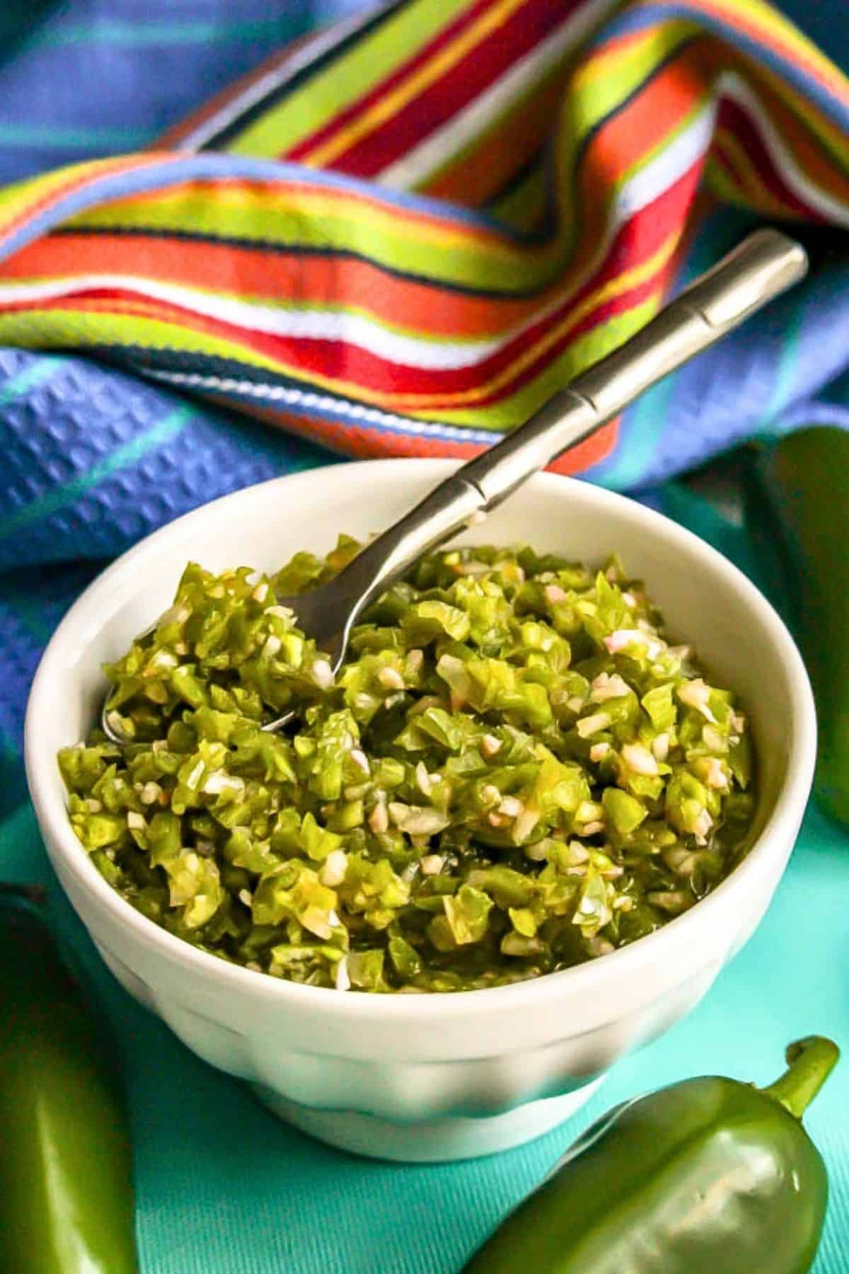 A small white bowl with a fresh homemade jalapeño pepper relish with a small serving spoon resting in it.