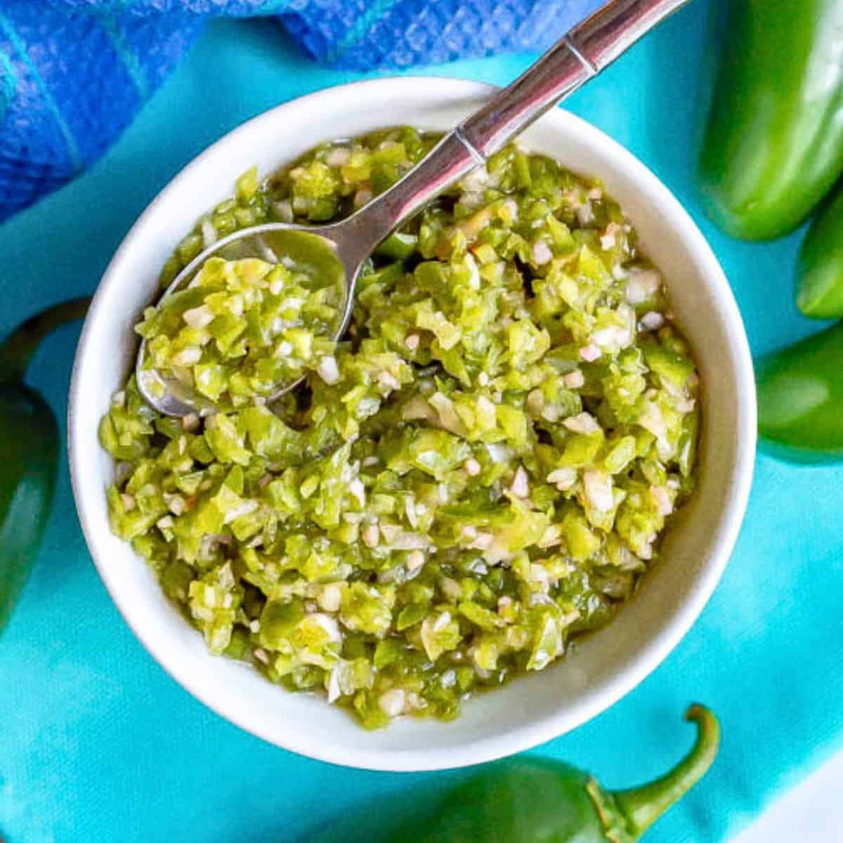 A small white bowl with a fresh homemade jalapeño relish with a small serving spoon resting in it.