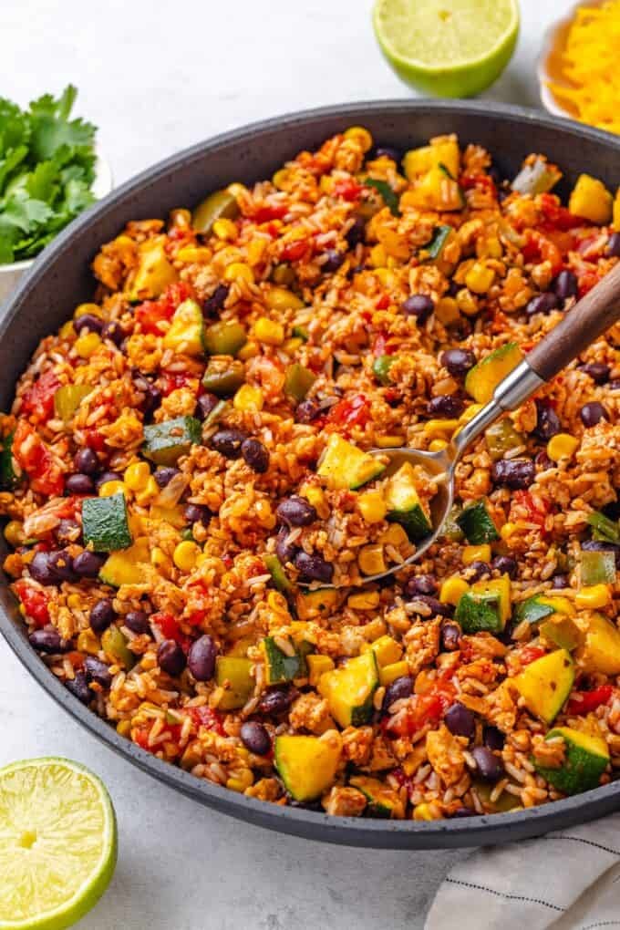 A spoon scooping up some rice and beans with ground turkey and veggies from a skillet.