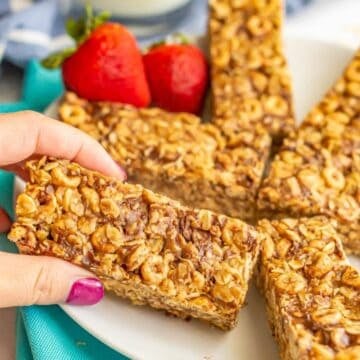 Close up of a hand picking up a no bake oat and cereal breakfast bar from a plate of bars.