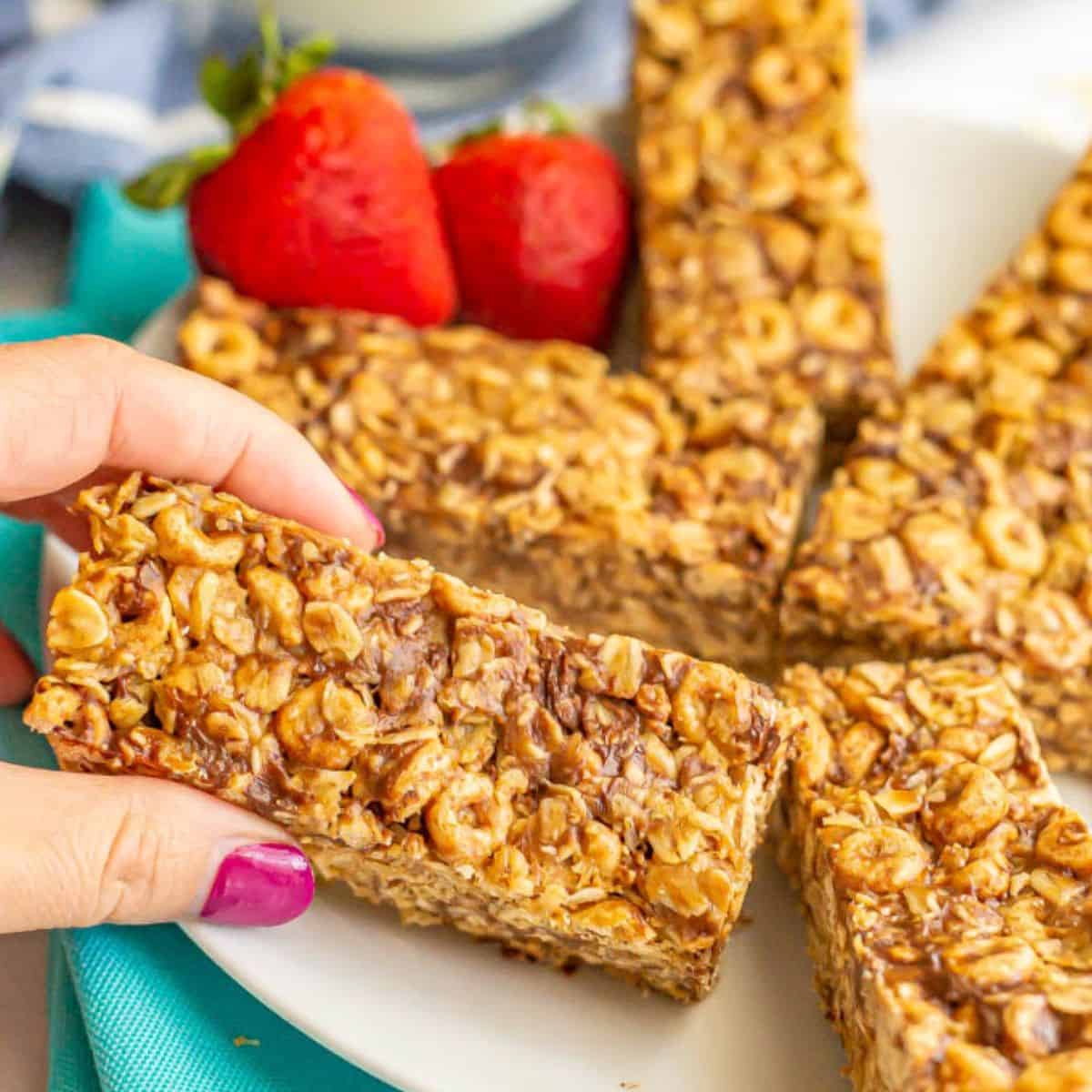 Close up of a hand picking up a no bake oat and cereal breakfast bar from a plate of bars.
