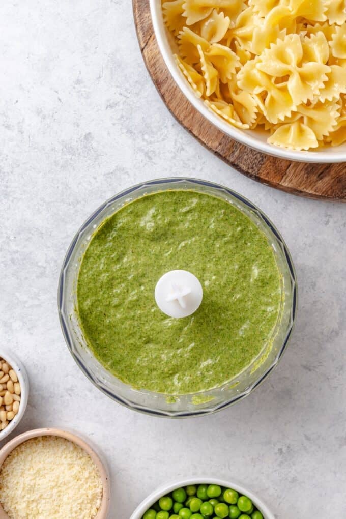 A food processor with a blended pesto and spinach mixture.