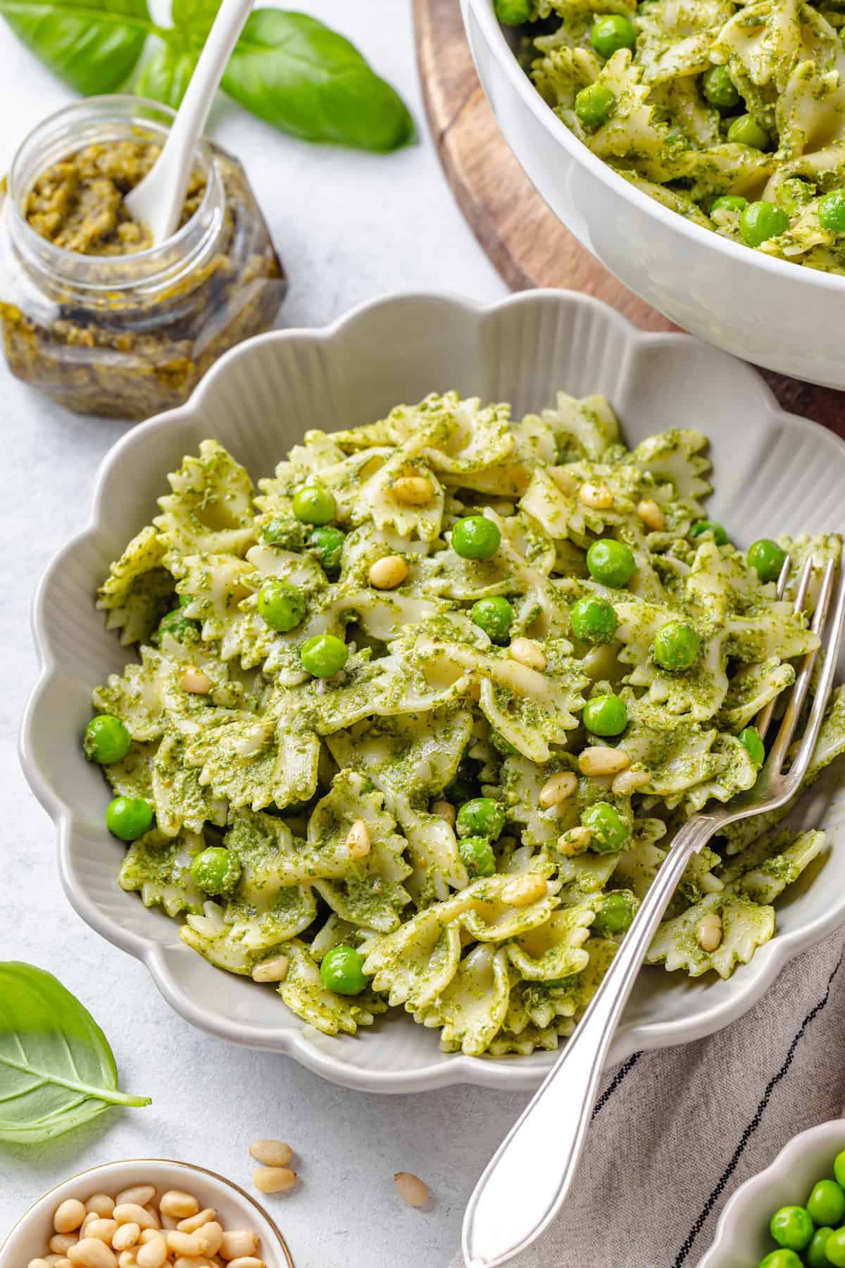 A fluted serving bowl with pasta, pesto and peas mixture with a fork resting to the side.