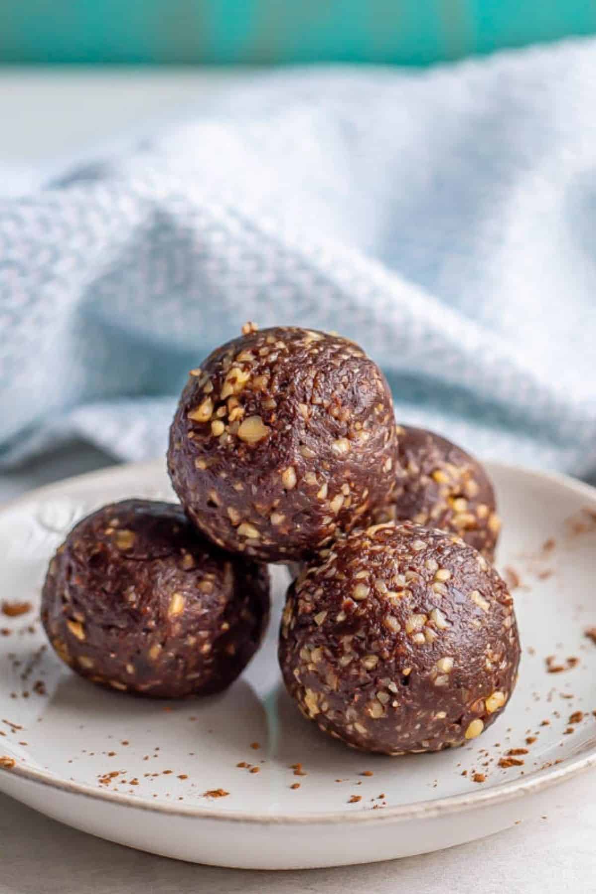 Homemade brownie energy bites with dates and walnuts stacked on a plate with cocoa powder dusted on it.