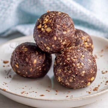 Close up of homemade brownie energy bites with dates and walnuts stacked on a plate with cocoa powder dusted on it.