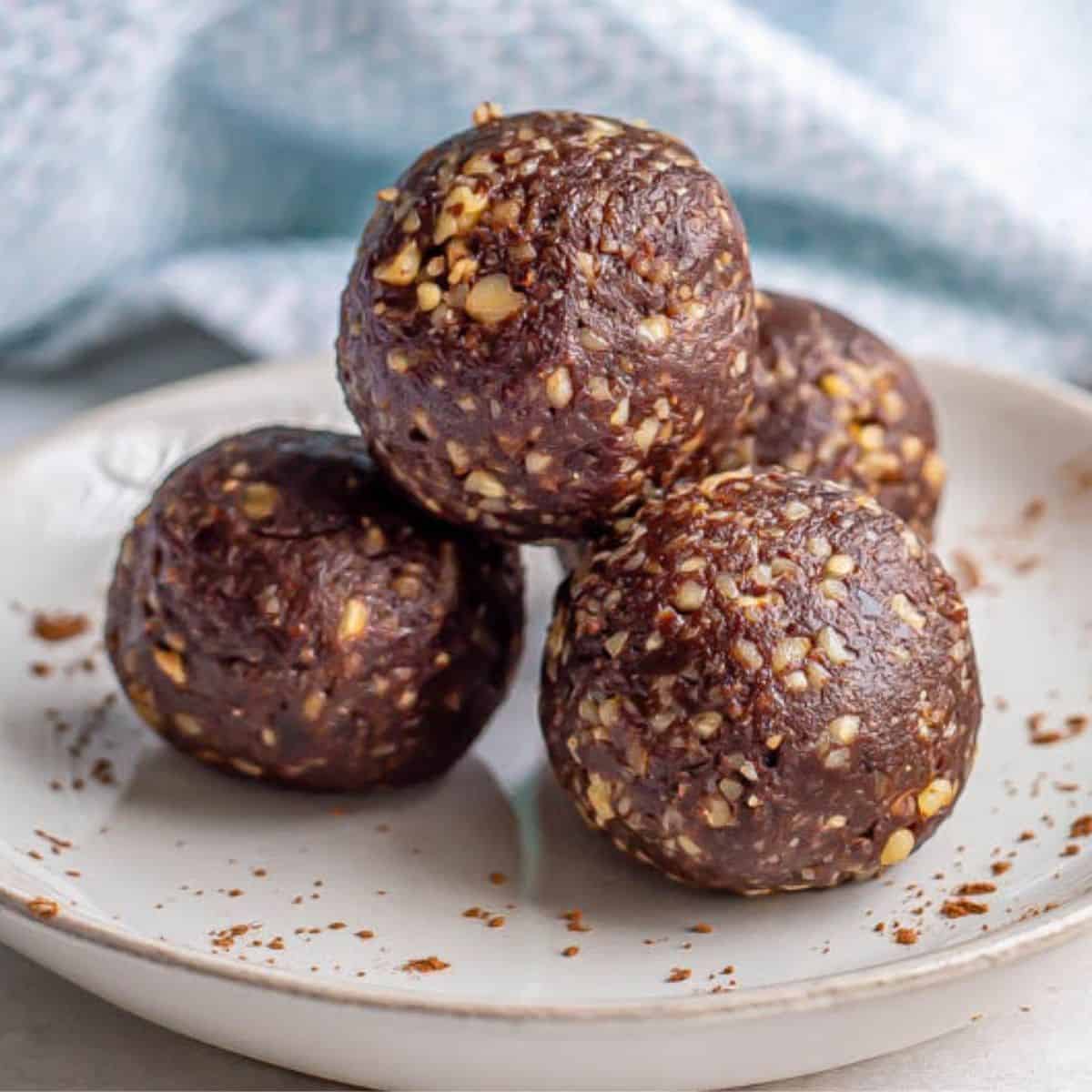 Close up of homemade brownie energy bites with dates and walnuts stacked on a plate with cocoa powder dusted on it.