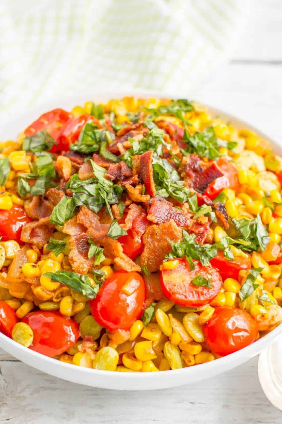 A serving bowl full of a corn and lima bean succotash with tomatoes, basil and bacon.