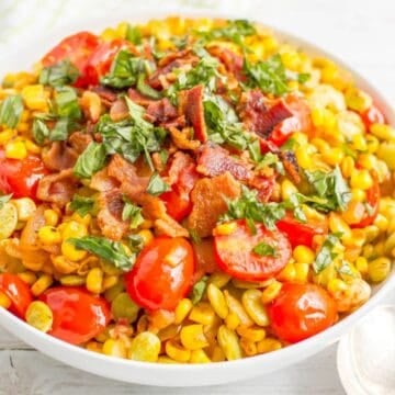 Close up of a serving bowl full of a corn and lima bean succotash with tomatoes, basil and bacon.