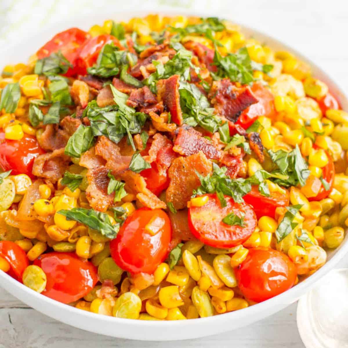 Close up of a serving bowl full of a corn and lima bean succotash with tomatoes, basil and bacon.
