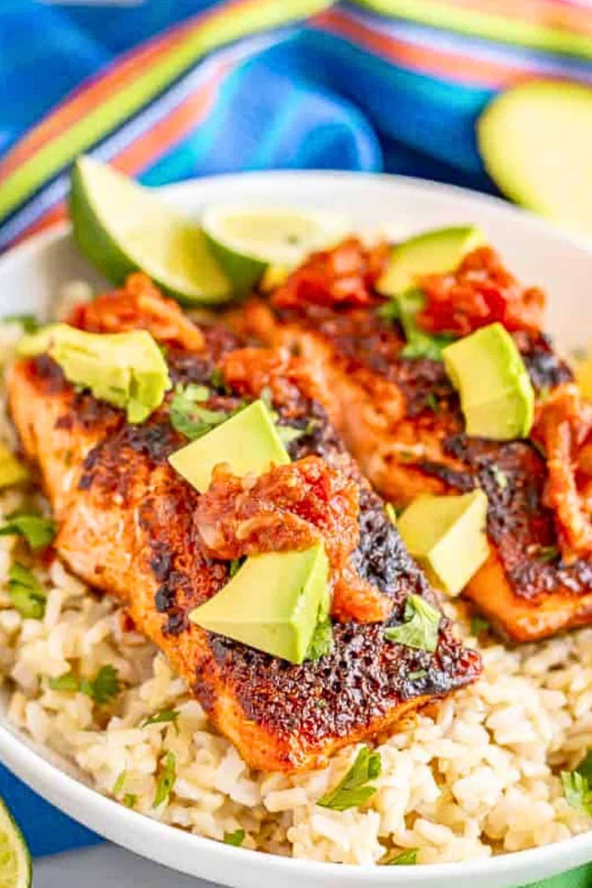 Two filets of baked southwest salmon served on a bed of rice with salsa, avocado and cilantro as toppings.