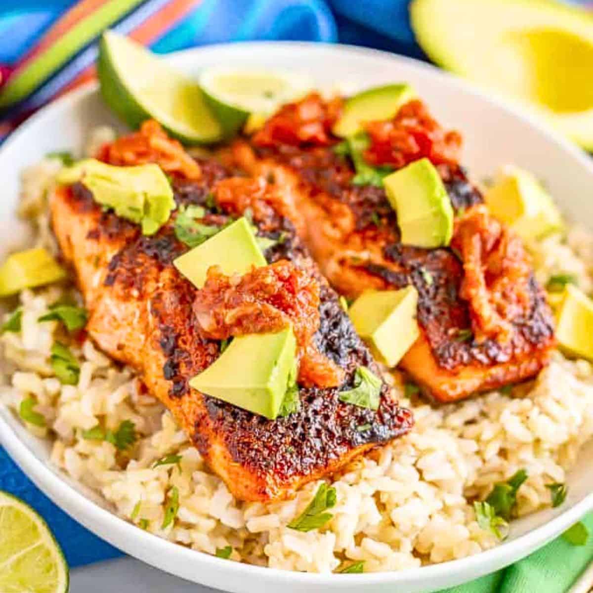 Close up of two filets of roasted southwest salmon served on a bed of rice with salsa, avocado and cilantro as toppings.
