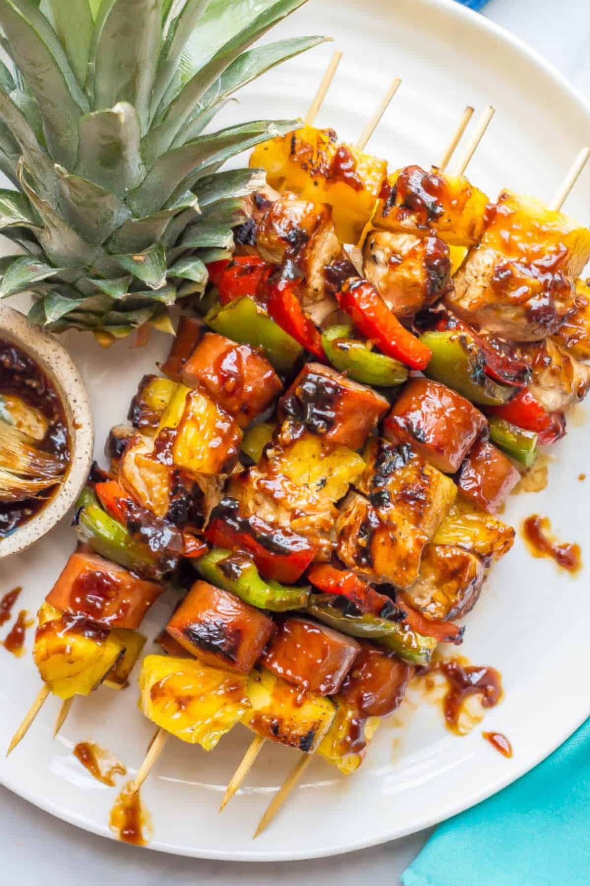 A serving plate with stacked kabobs with chicken, sausage, pepper and pineapple pieces brushed with teriyaki sauce.