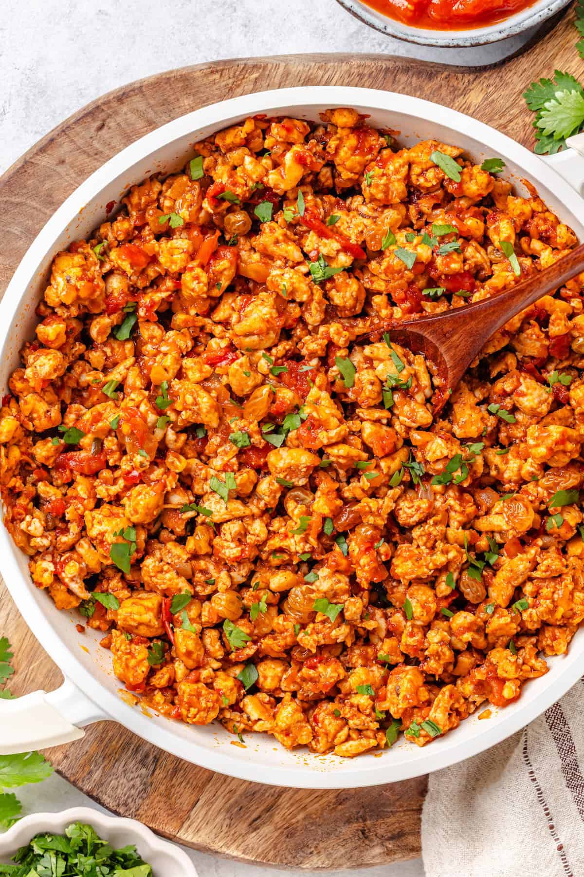 A quick chicken picadillo skillet with raisins and cilantro and a wooden spoon resting in the dish.