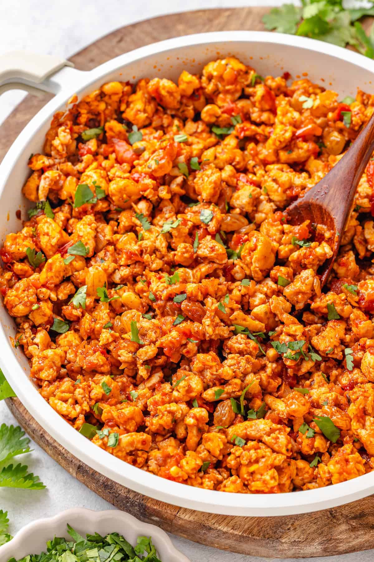 A ground chicken picadillo mixture with raisins and cilantro and a wooden spoon resting in the skillet.