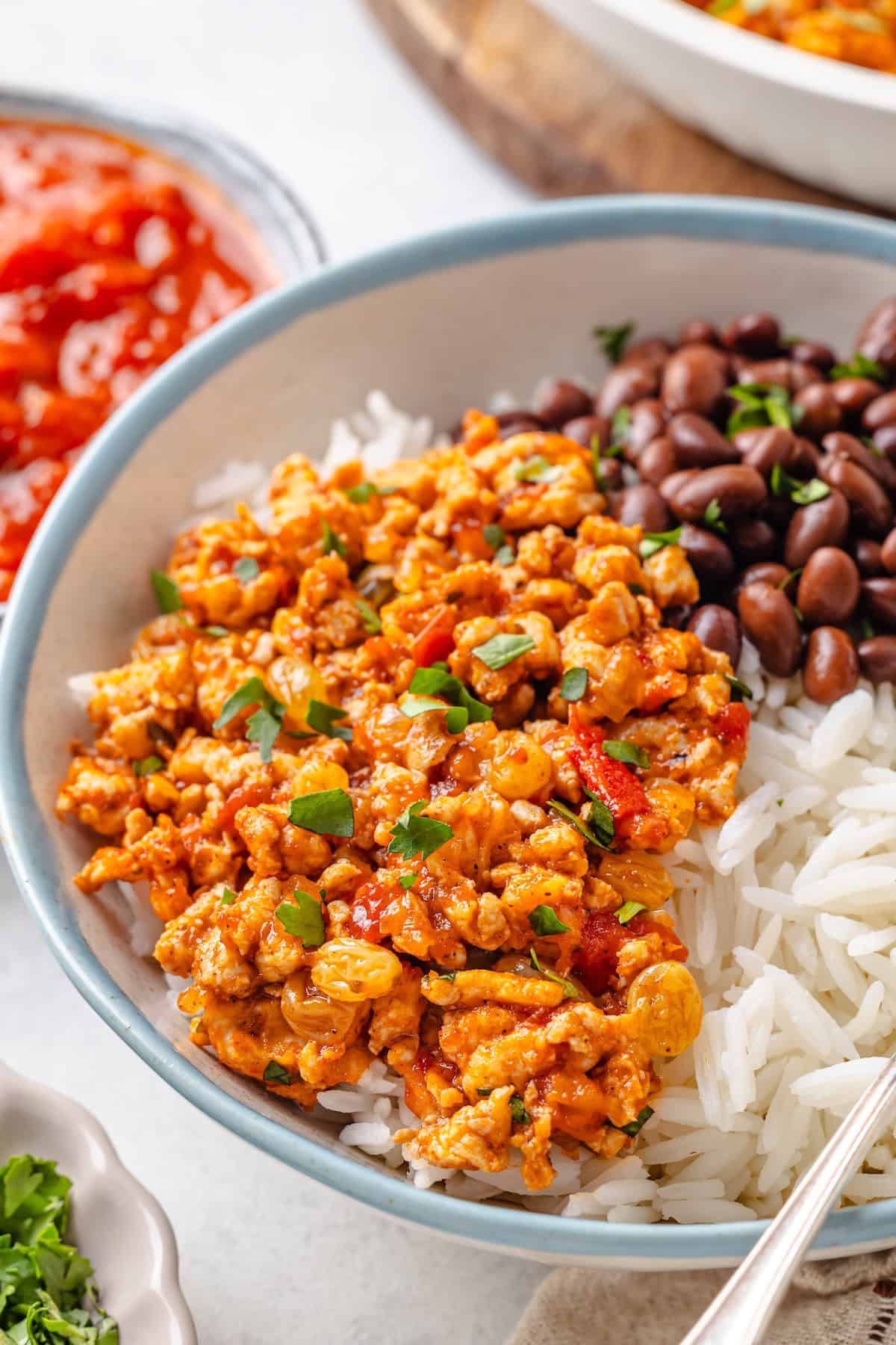 A scoop of chicken picadillo served over white rice alongside black beans.