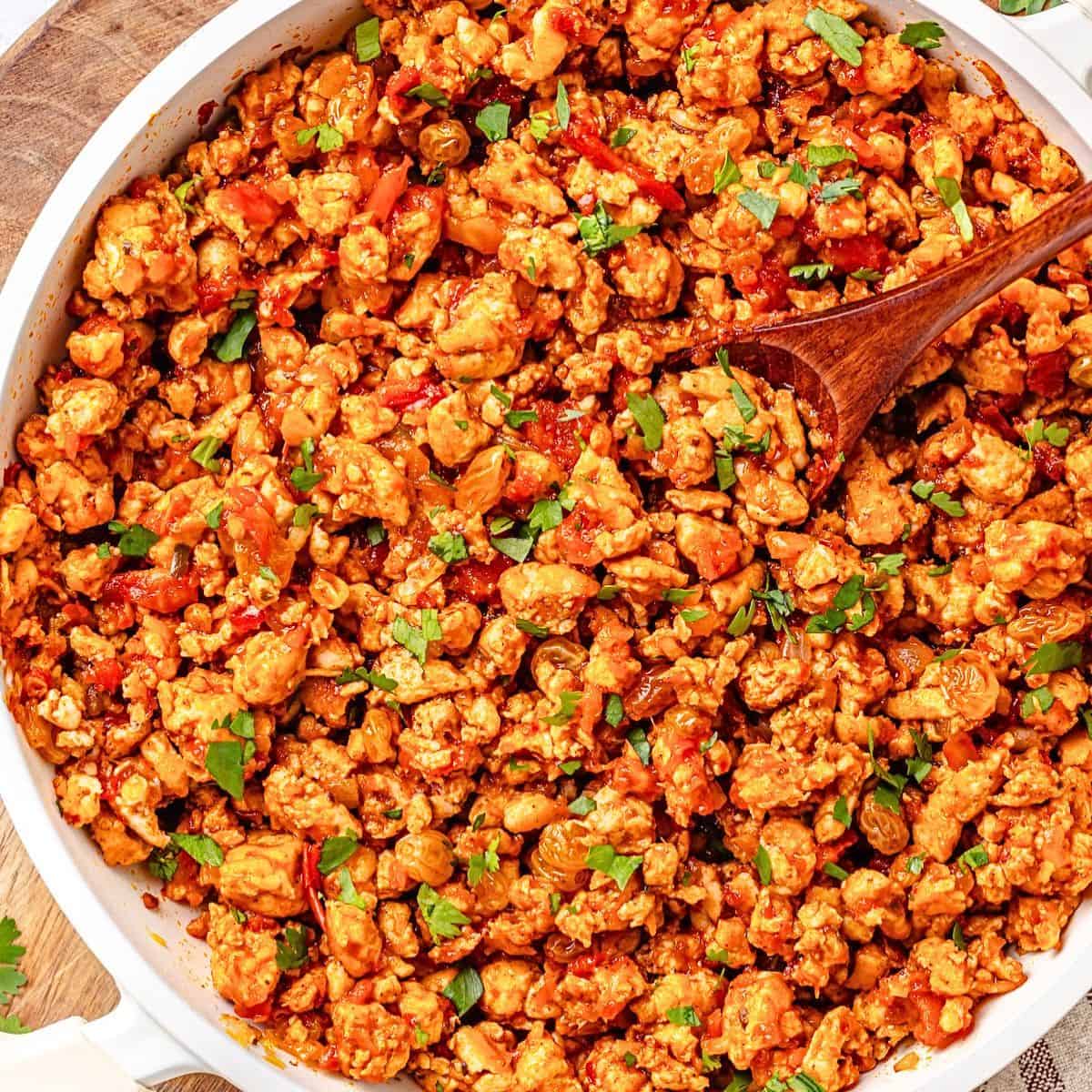 Close up of a quick chicken picadillo skillet with raisins and cilantro and a wooden spoon resting in the dish.
