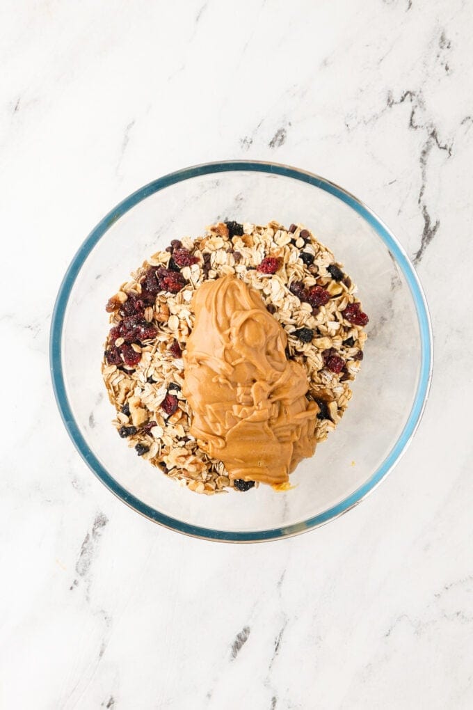 A creamy peanut butter honey mixture added on top of oats and dried fruit in a glass bowl.