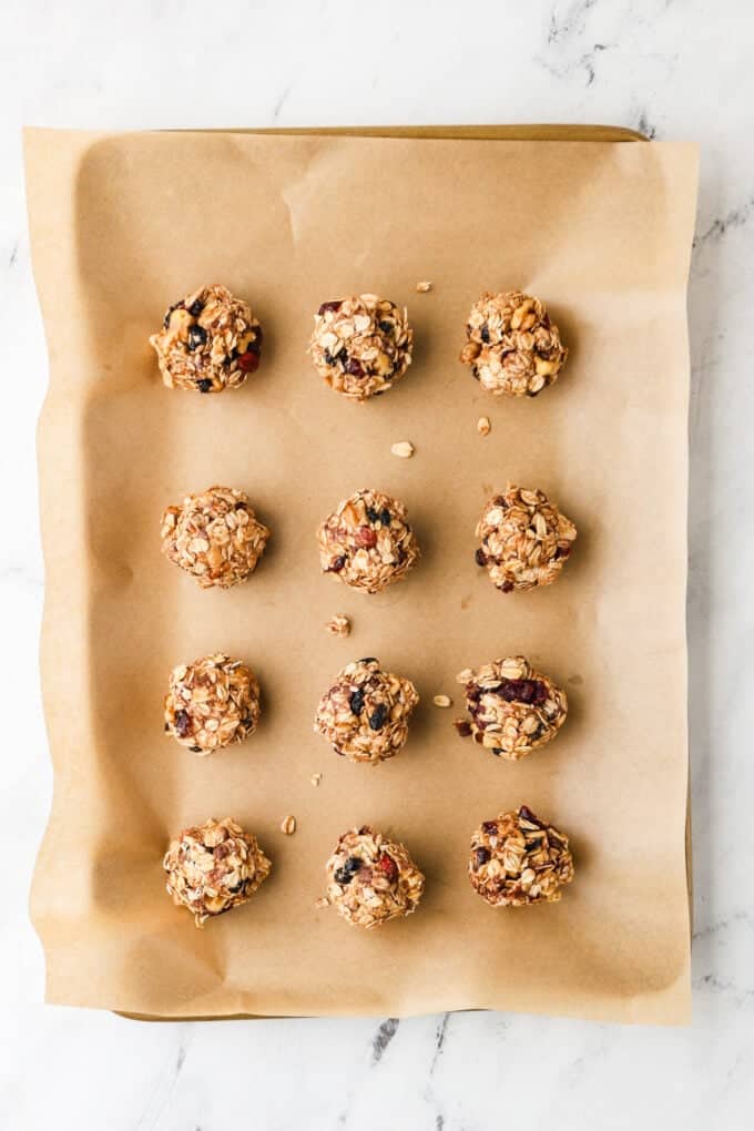 Rolled granola balls with dried fruit and mini chocolate chips on a parchment paper lined baking sheet.