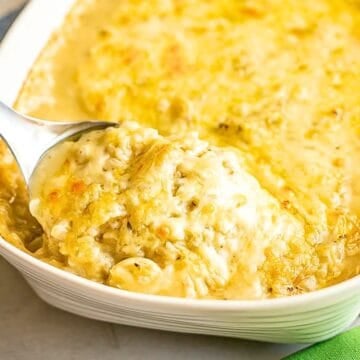 Close up of a scoop of a cheesy chicken and rice casserole being lifted from a white rectangular baking dish.