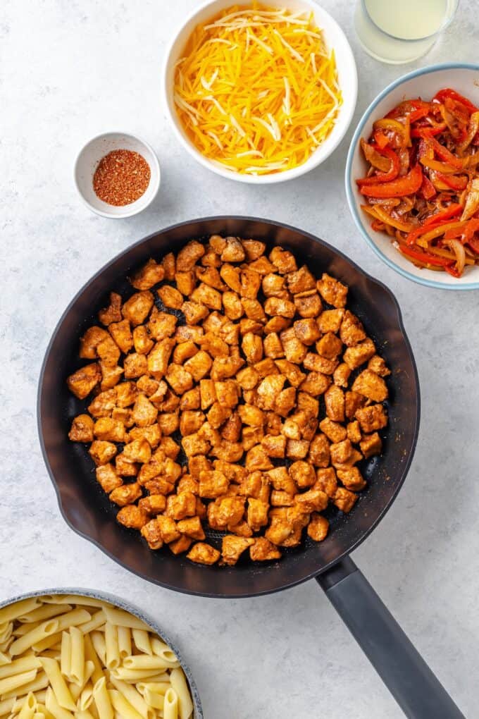 Cooked cubed chicken pieces with fajita seasoning in a cast iron skillet.