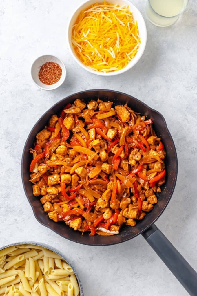 A cast iron skillet with a fajita mix of sautéed onions and peppers and cubed chicken pieces.
