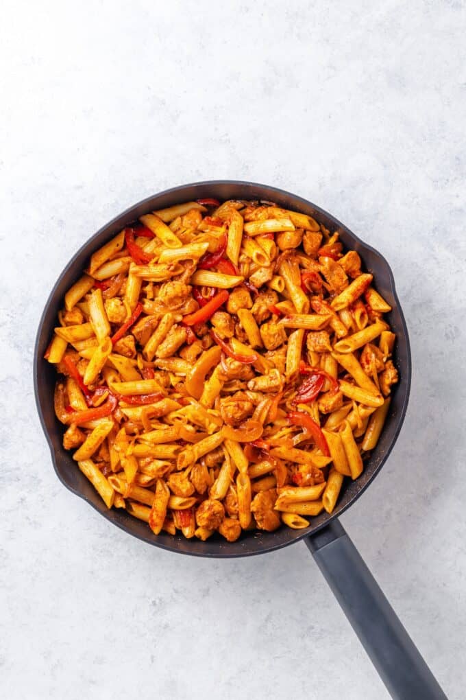 A cast iron skillet with a cheesy fajita chicken pasta mixture with onion and bell peppers.