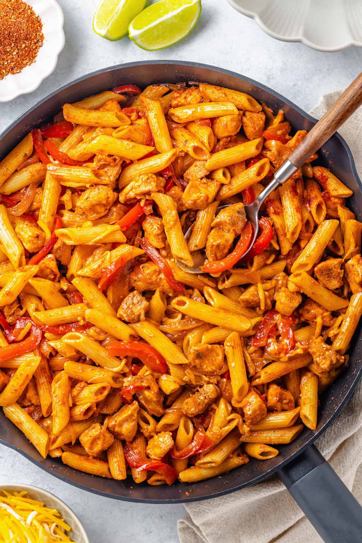 Close up of a spoon resting in a cast iron skillet filled with a fajita chicken pasta mixture.