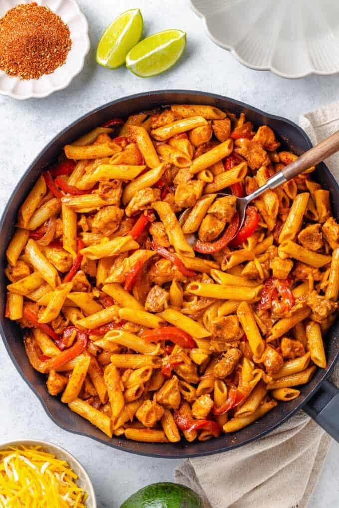 A spoon resting in a cast iron skillet filled with a fajita chicken pasta mixture.