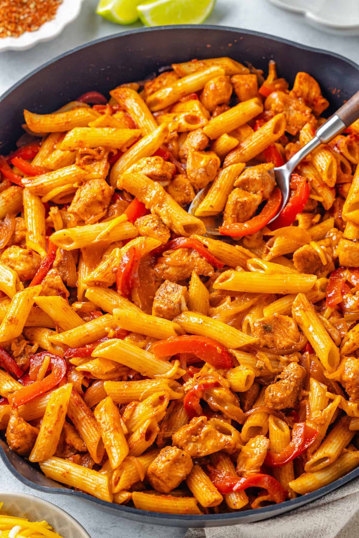 Penne pasta with fajita chicken, onion and peppers in a cast iron skillet.