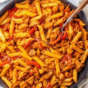 Cropped close up of a spoon resting in a cast iron skillet filled with a fajita chicken pasta mixture.