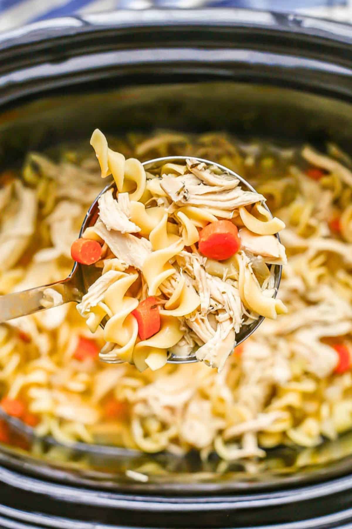 A ladle full of chicken noodle soup being lifted from a slow cooker insert.