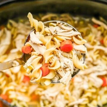 Close up of a ladle full of chicken noodle soup being lifted from a slow cooker insert.