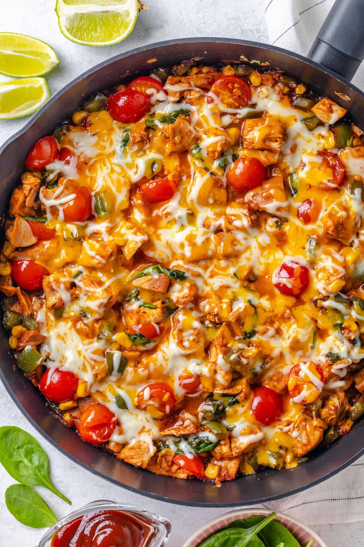 A BBQ chicken skillet with spinach and tomatoes and melted cheese on top.