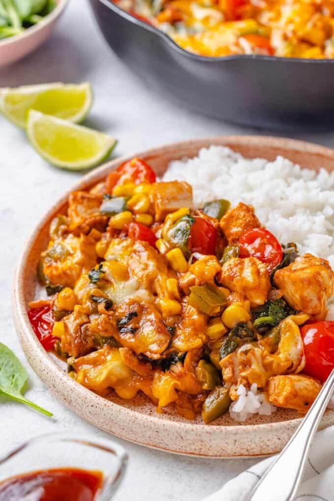 BBQ chicken with corn, spinach and tomatoes served alongside rice on a dinner plate.