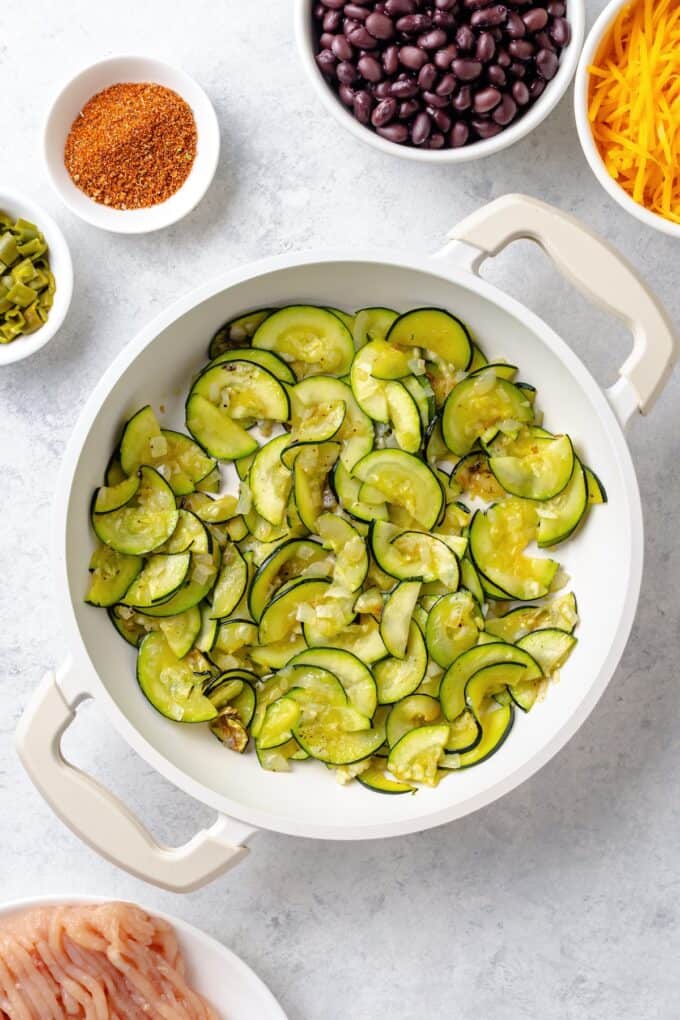Sliced zucchini being sautéed in a white skillet.