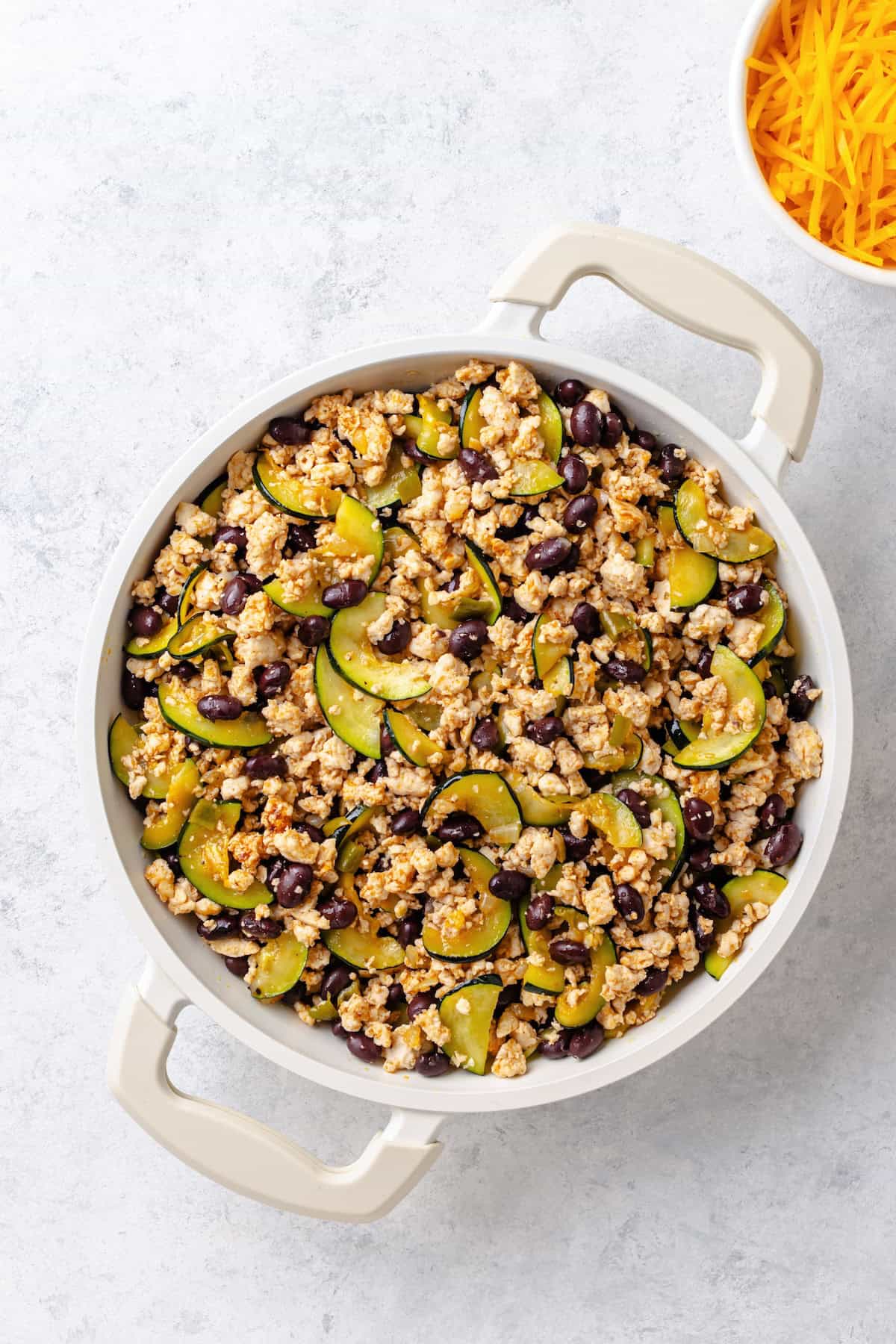 A large white skillet with a mixture of ground turkey and zucchini with black beans.