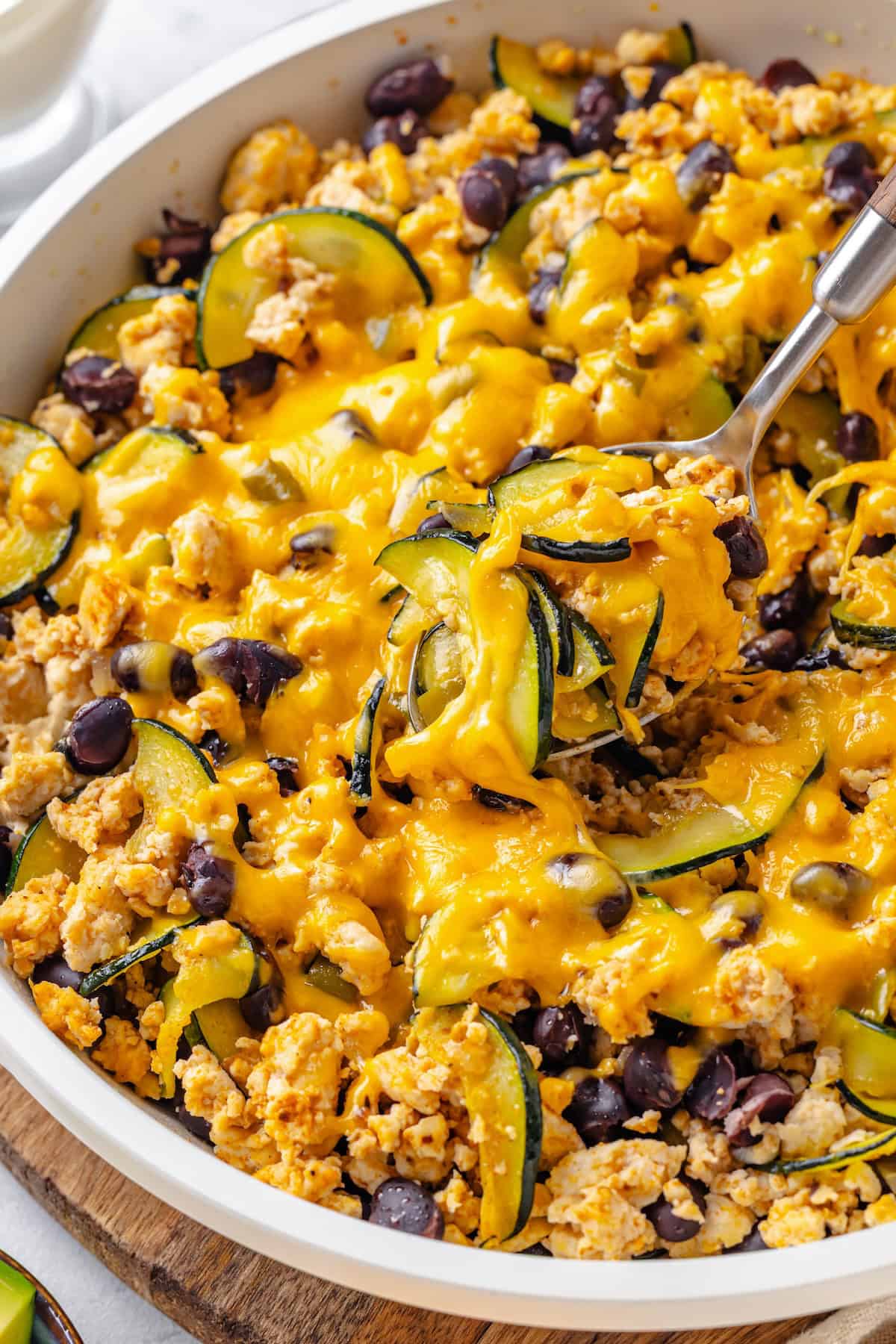 A spoon lifting out a scoop of a ground turkey skillet with zucchini and black beans and melted cheese on top.