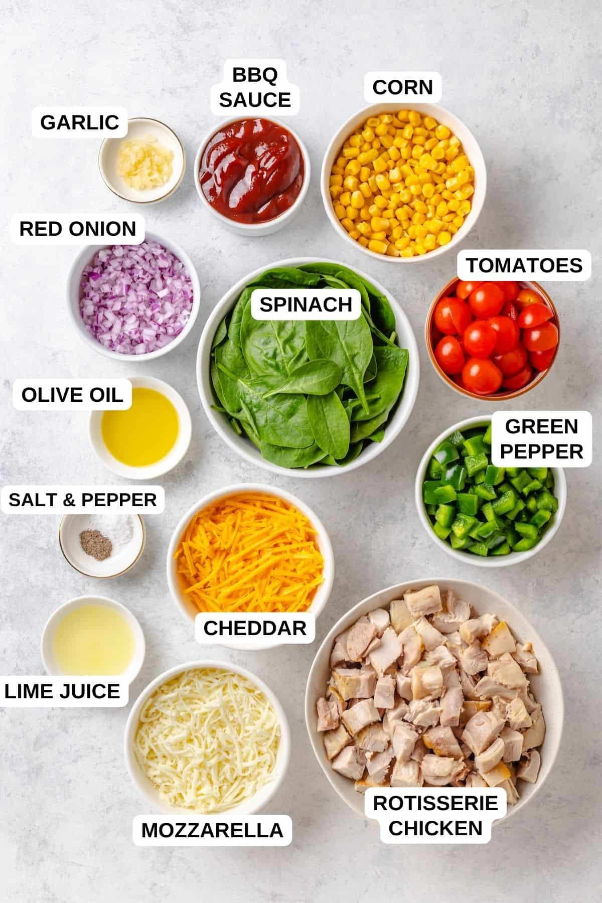 Ingredients laid out in separate bowls for making a BBQ chicken recipe with red onion, corn, spinach, tomatoes and cheese.