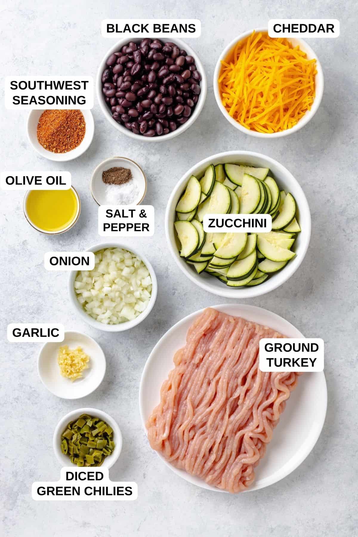 Ingredients laid out in separate bowls for making a ground turkey recipe with zucchini, black beans and cheddar cheese.