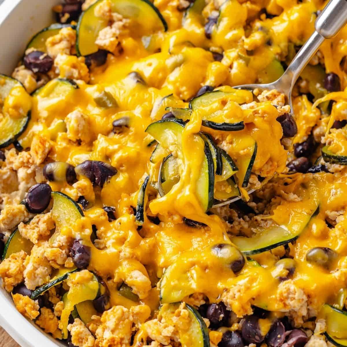 Close up of a spoon lifting out a scoop of a ground turkey skillet with zucchini and black beans and melted cheese on top.