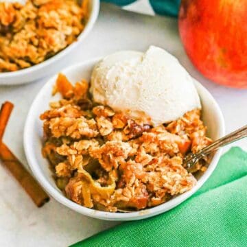 A spoon resting in a bowl of vanilla ice cream topped apple crisp